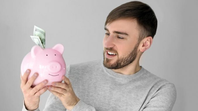 Happy young man holding piggy bank with money at home