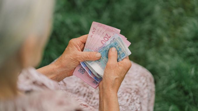 Concerned elderly woman counting Ukrainian money hryvnia.