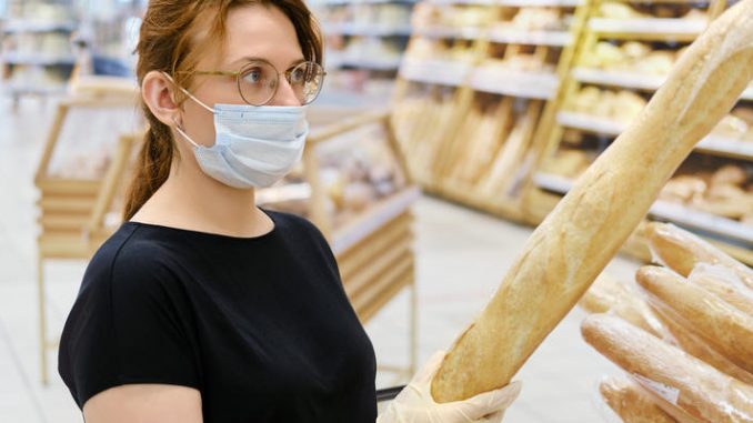 Red-haired girl in a medical mask buys bread in a supermarket