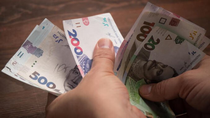 Caucasian man counts paper money. Male hands holding pack of new Ukrainian banknotes, hryvnias on wooden table. Cash money concept. Investment concept. Close up shot