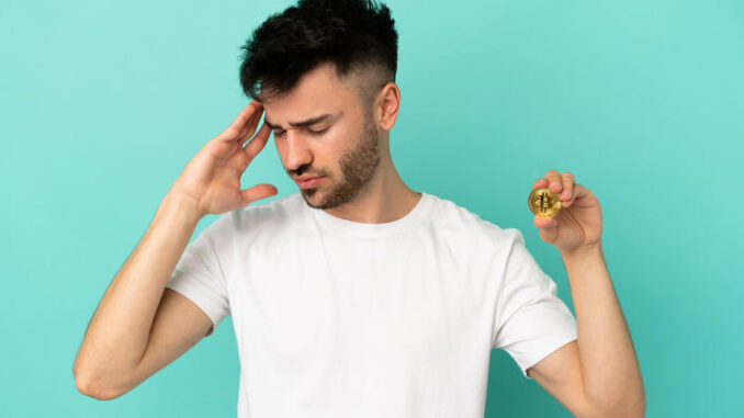 Young man holding a Bitcoin isolated on blue background with headache